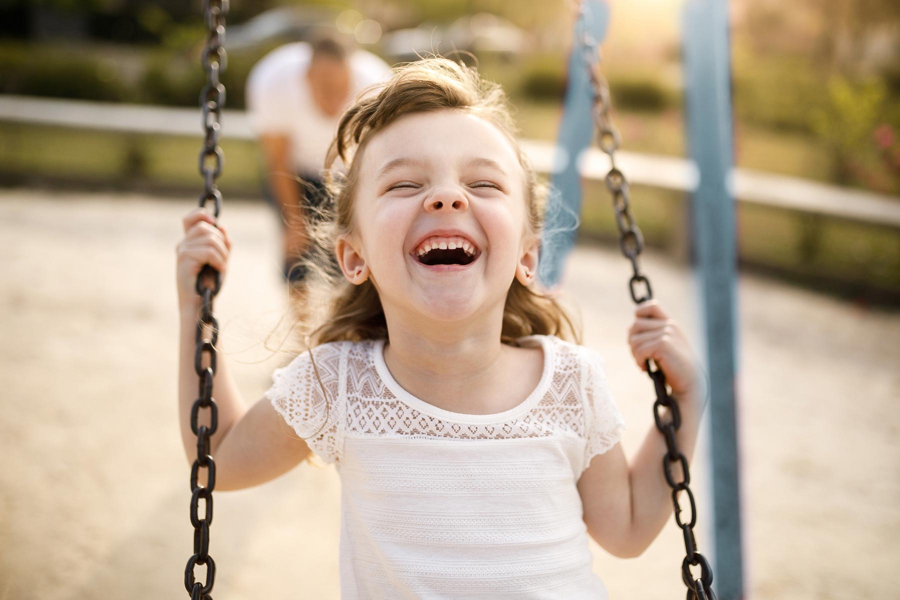 Young girl laughing joyfully while holding onto the chains of a playground swing outdoors